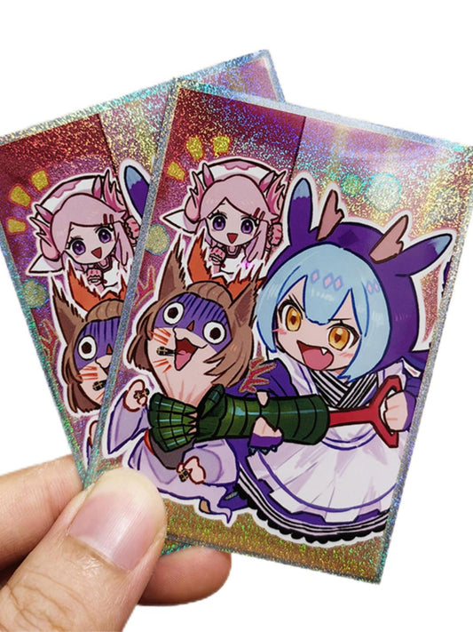 Three holographic anime trading cards featuring chibi characters, held in a person's hand against a plain white background.