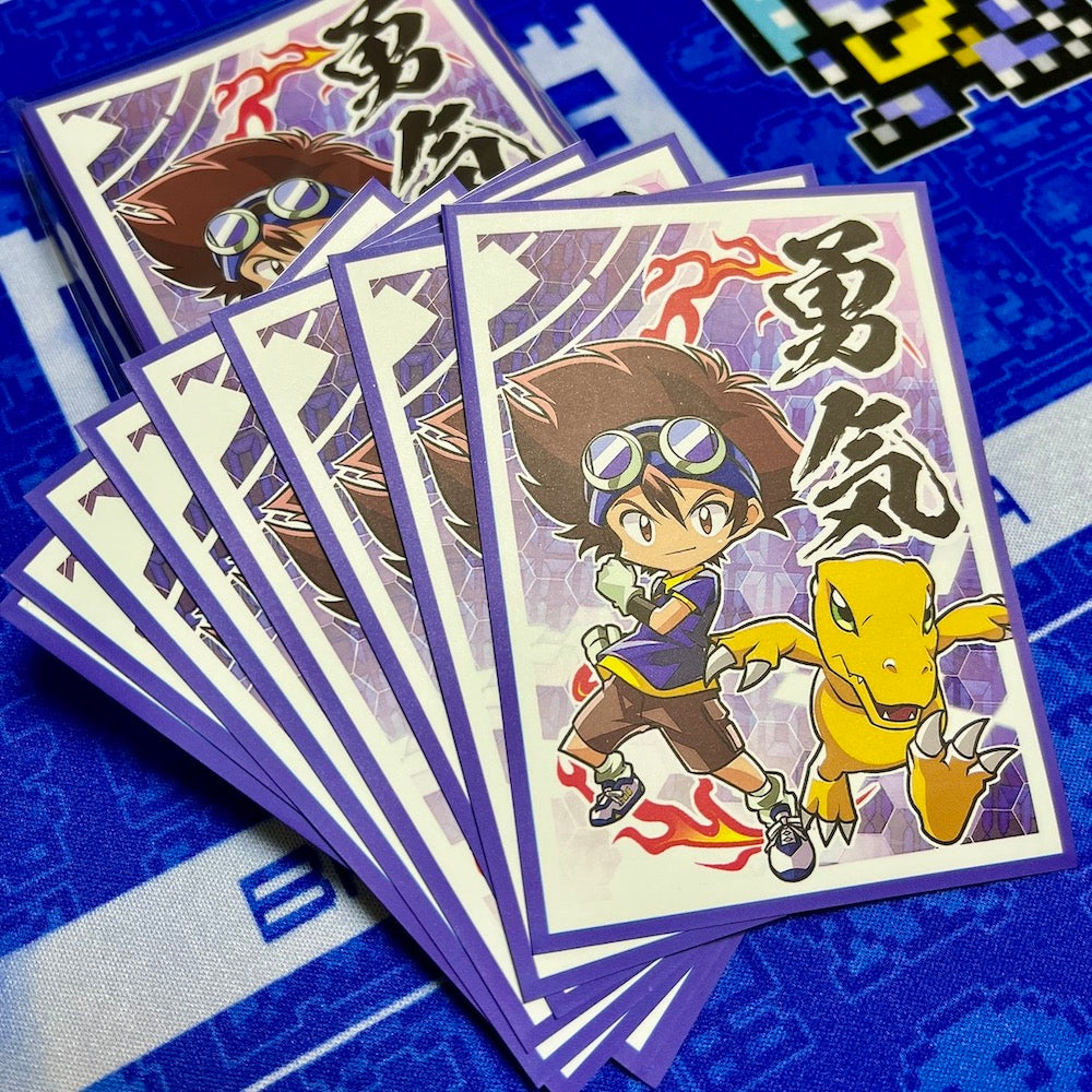A fan of illustrated trading cards or sticker cards showing a chibi anime character with goggles and a yellow dinosaur-like companion, photographed on a blue patterned surface.
