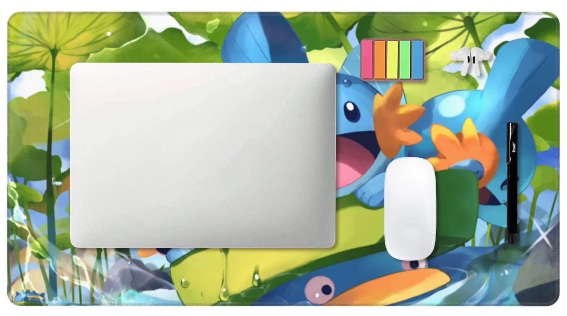 A rectangular desk mat with a colorful cartoon frog and lily pad design, shown with a closed silver laptop, a white mouse, and a black stylus on top against a white background.