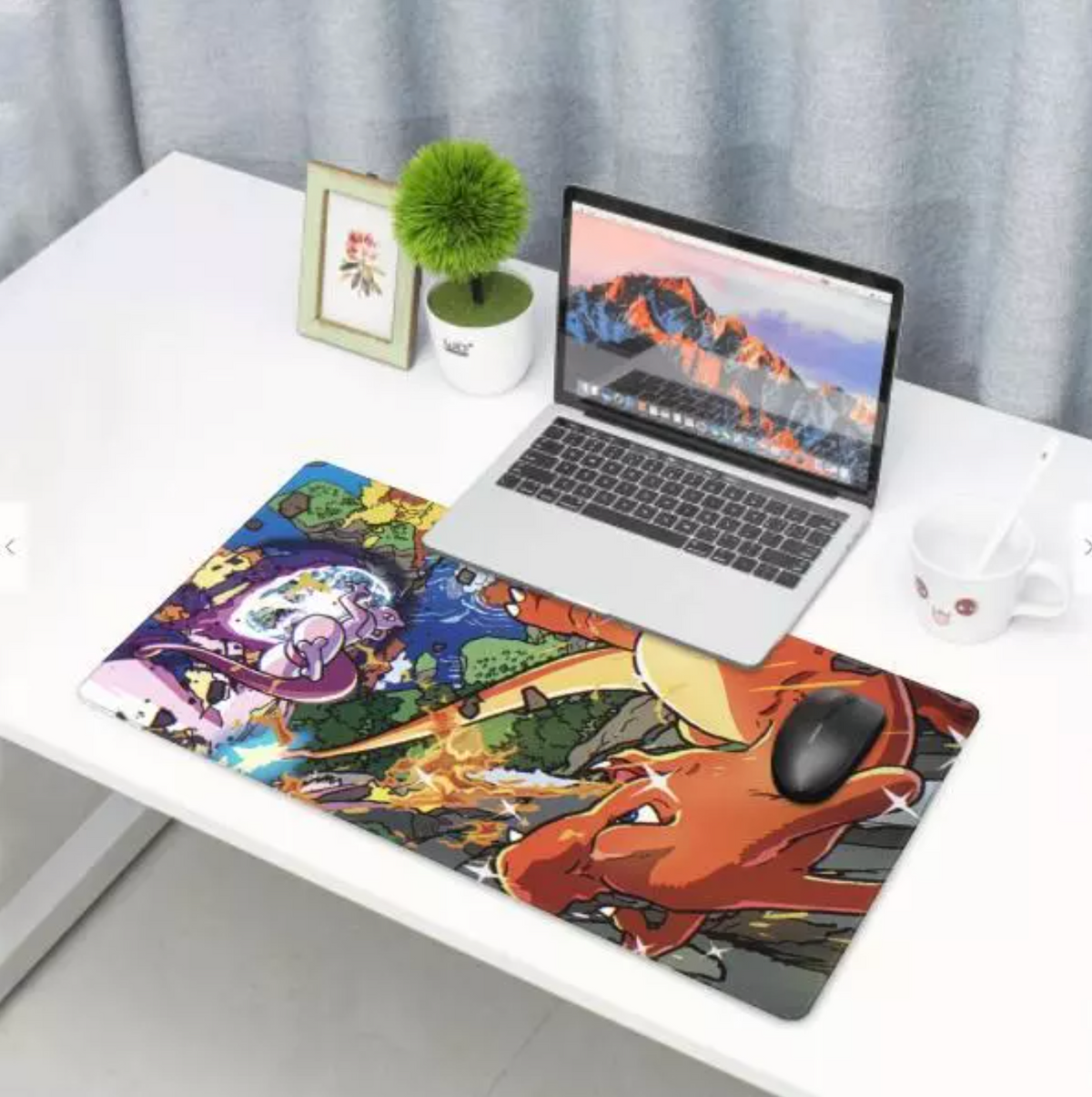 A large rectangular desk mat with a colorful anime-style illustration lies on a white desk next to an open silver laptop, a small potted plant, a framed picture, and a white mug.